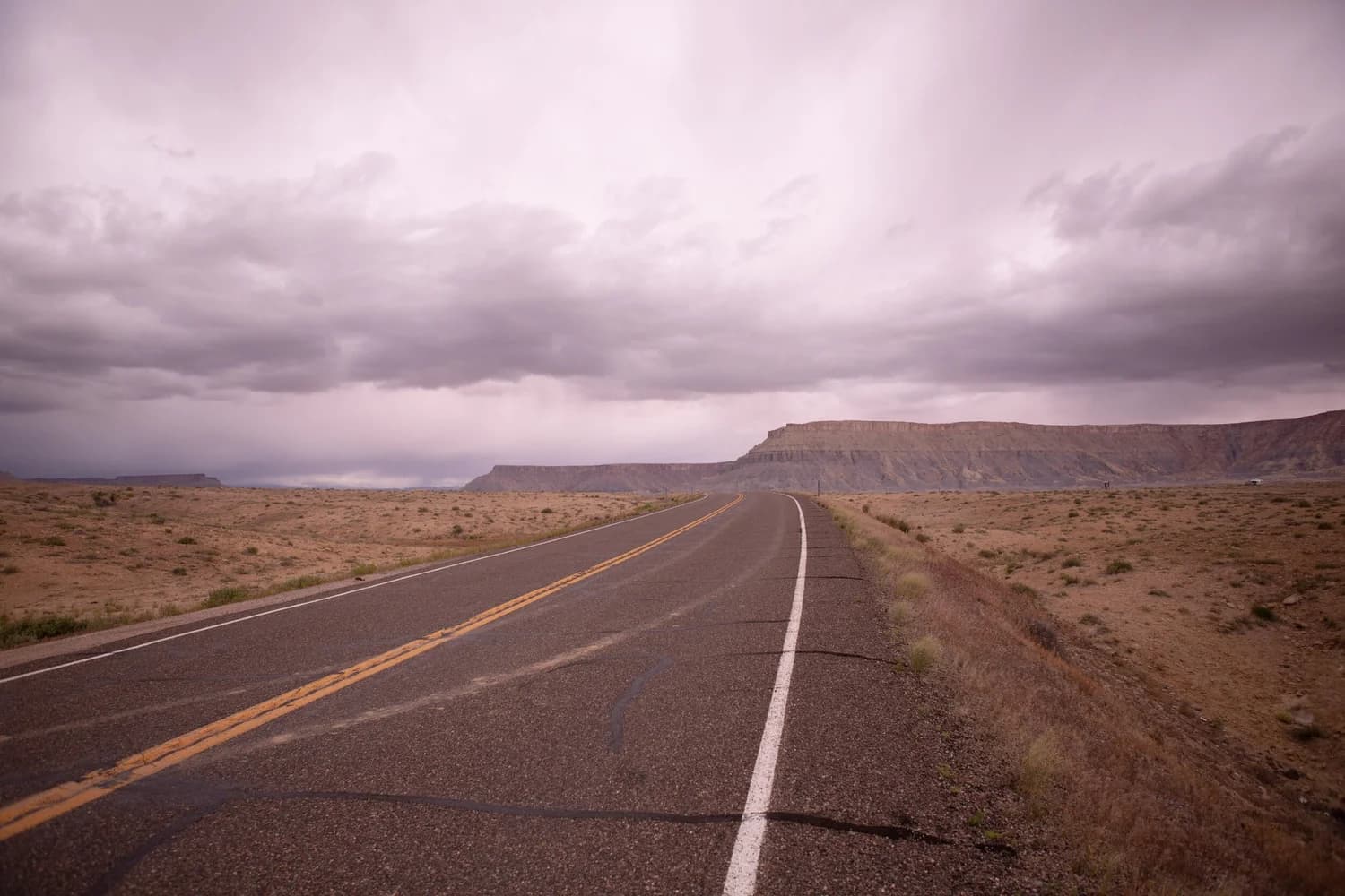 A desert highway stretching toward mesas under heavy storm clouds