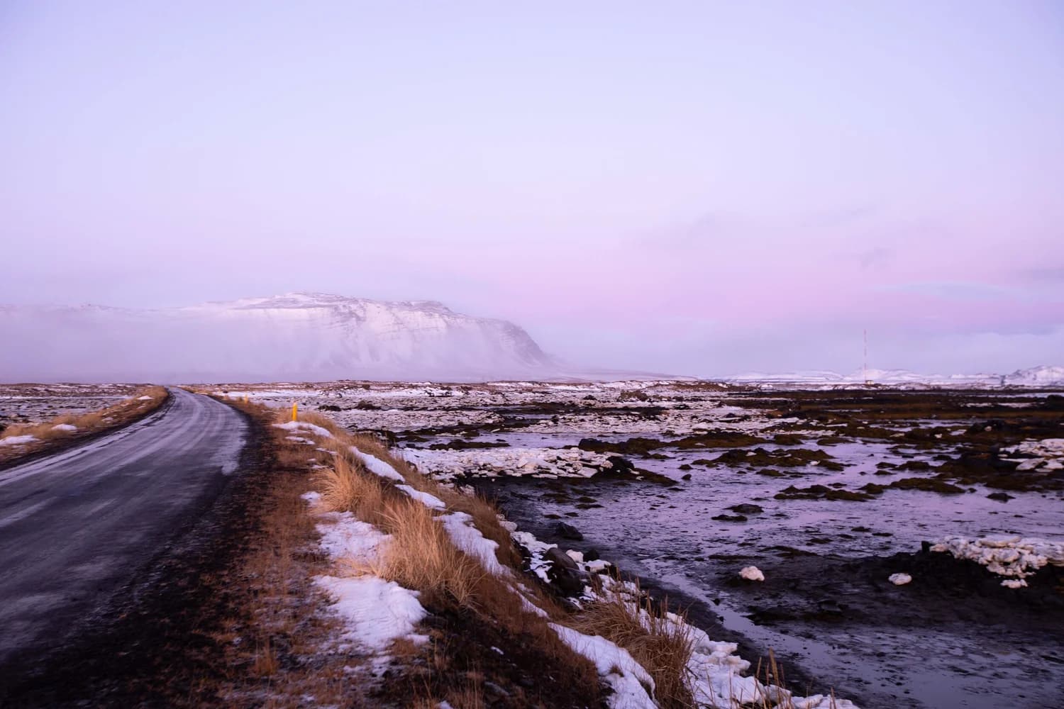 A road crossing a snowy plateau beneath a lavender sky