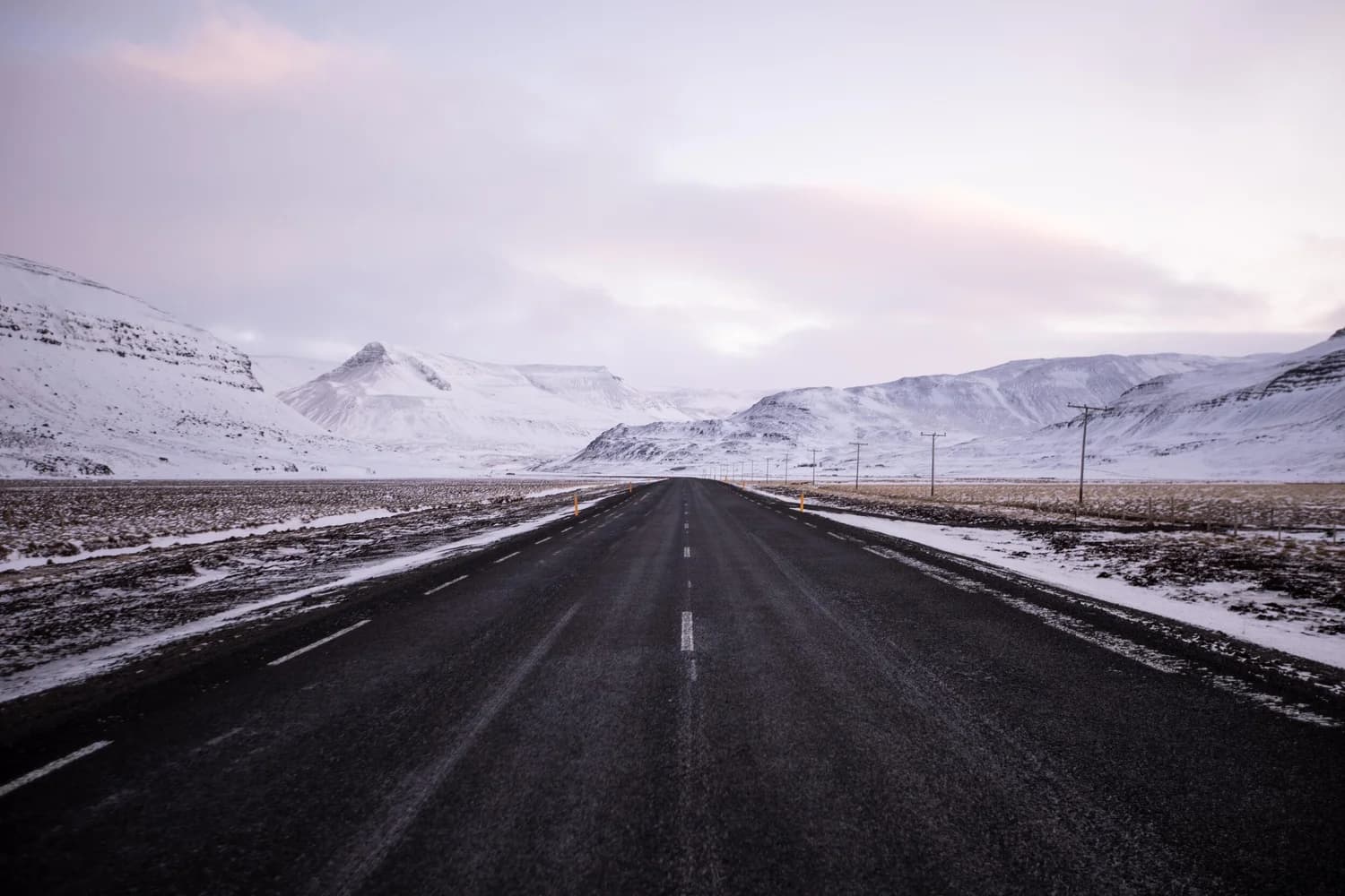 An open road running toward snow-covered mountains under a pale sky