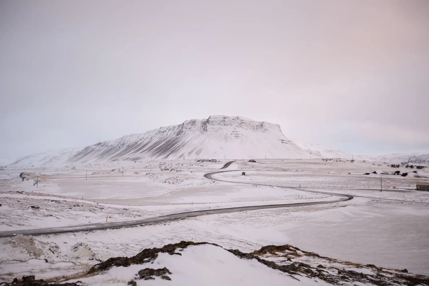 A quiet road curving across a snow-covered plain toward a flat-topped mountain